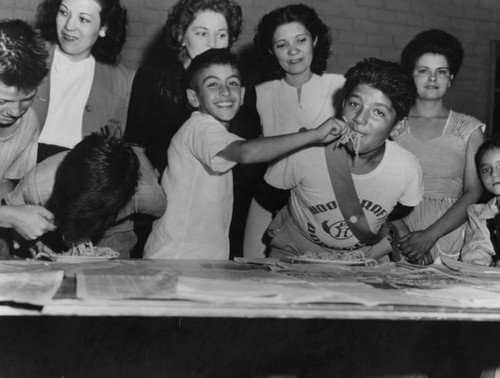 Woodcraft Rangers at Aliso Village in Boyle Heights, CA participate in a spaghetti eating contest. A young boy with a mouthful of spaghetti gets fed by his partner. Los Angeles Public Library Photo Collection.