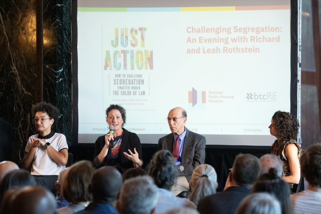 ASL interpreter Makeda Duncan, Leah Rothstein, Richard Rothstein, and Marisa Novara sit in a row in front of a screen. The screen has a photo of the book "Just Action" on it along with logos for the National Public Housing Museum and btcRE.