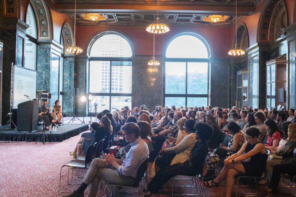 A crowd sits in the Chicago Cultural Center's G.A.R. Hall, an ornate room with soaring ceilings and large windows.