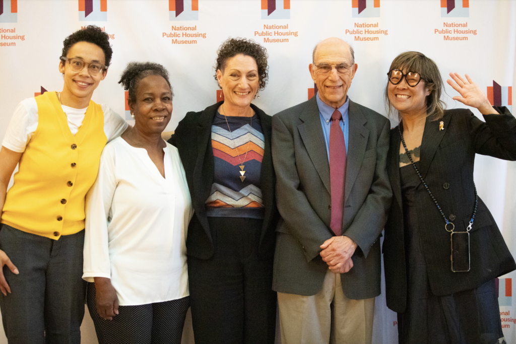 Authors Richard and Leah Rothstein stand National Public Housing Museum Associate Director Tiff Beatty, Executive Director Lisa Sun Lee, and Board Member Deborah Bennett. They all stand in front a a branded white banner with small National Public Housing Museum logos repeated across it.