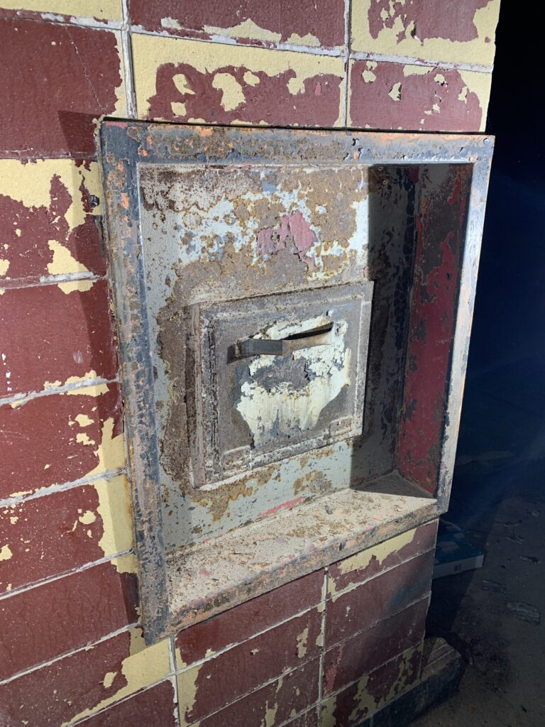 Rusted trash chute in a brick wall.