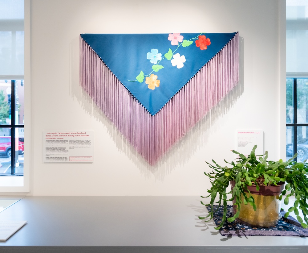 A shawl with flowers and long fringe displayed in a gallery