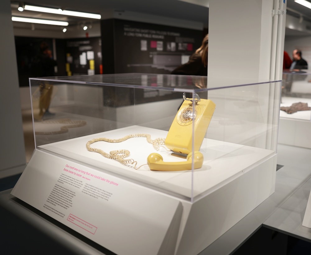 A yellow rotary phone in a display case