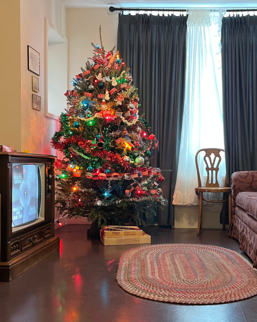 A Christmas tree decorated with holiday lights, paper loops, popcorn, and ornaments in a vintage apartment