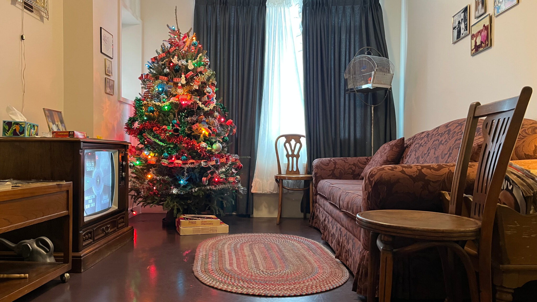 A Christmas tree decorated with holiday lights, paper loops, popcorn, and ornaments in a vintage apartment