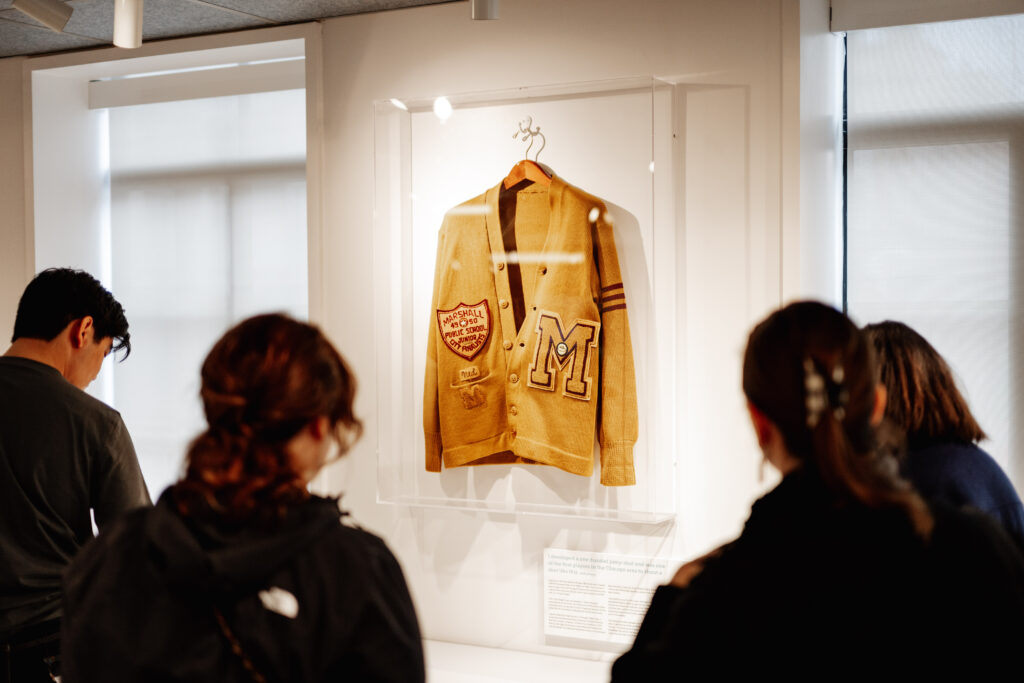 Museum visitors look at a midcentury high school letterman sweater
