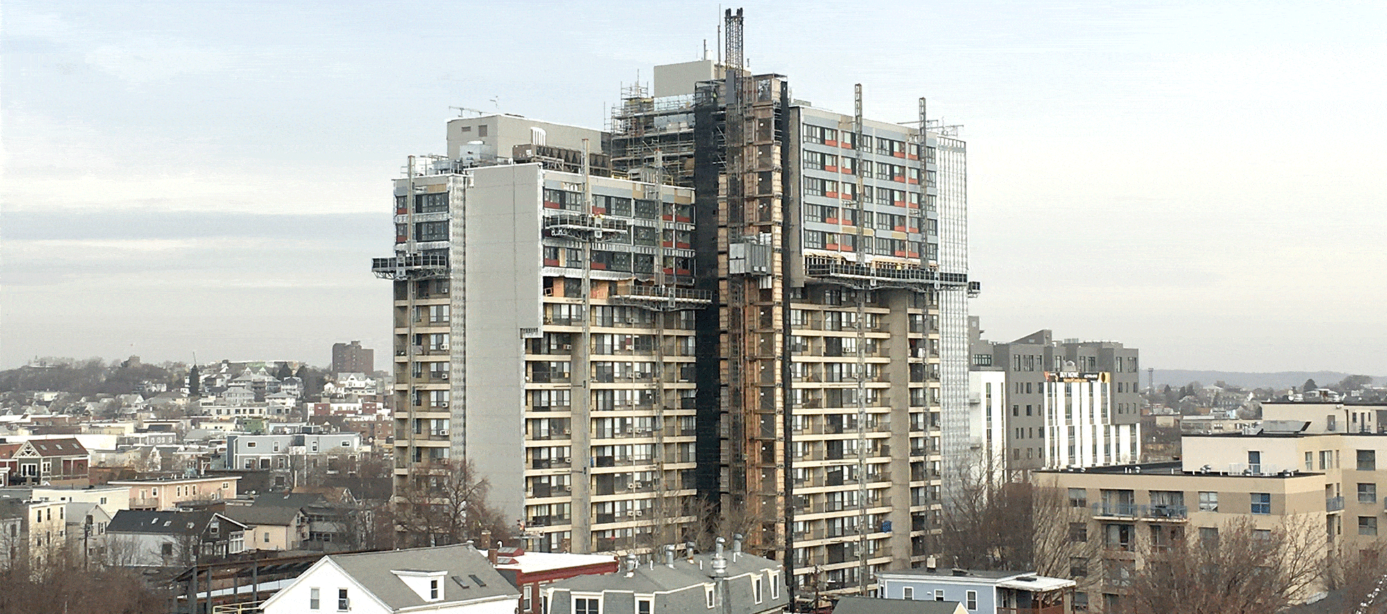 Landscape view centered on a high rise building, Millers River Apartments, undergoing renovation, with scaffolding surrounding it. Photo courtesy of Cambridge Housing Authority.