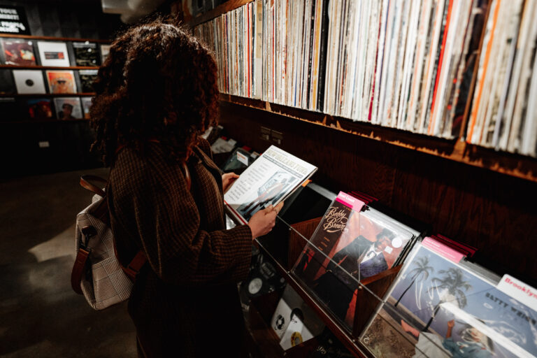 A person looks at an album cover while standing in front of shelves full of vinyl records