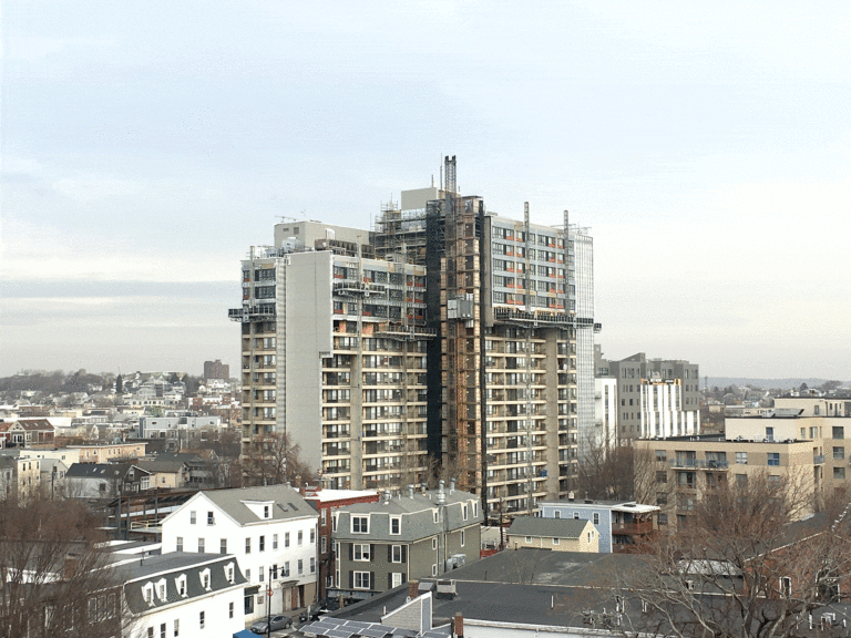 Landscape view centered on a high rise building, Millers River Apartments, undergoing renovation, with scaffolding surrounding it. [Cambridge Housing Authority]