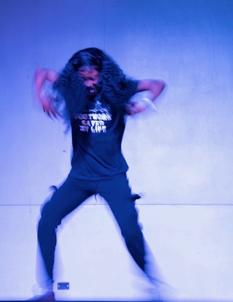 Blurry photo of a footwork dancer against a blue stage backdrop