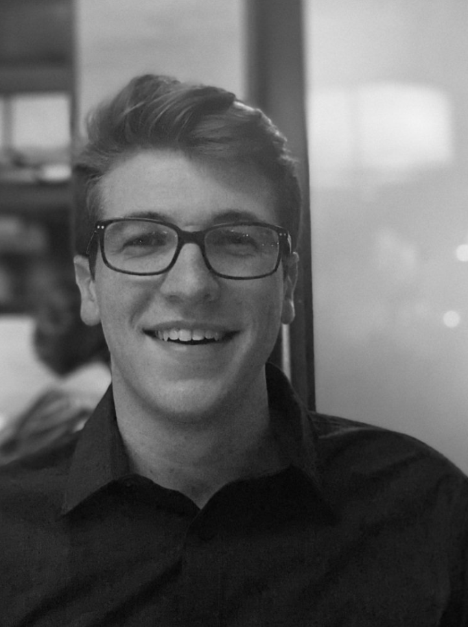 A black and white photo of Jack Werner. This photo shows Jack, a white man with pushed back blonde-ish hair, open mouth smiling. He is wearing a dark colored button up shirt.