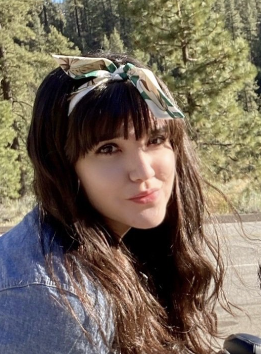 A photo of Victoria Límón. Victoria has an olive complexion and is wearing a jean jacket. She is framed in the bottom of the photo and is looking towards the camera. She has a cream, green, and brown head scarf tied up to her long, brown hair.