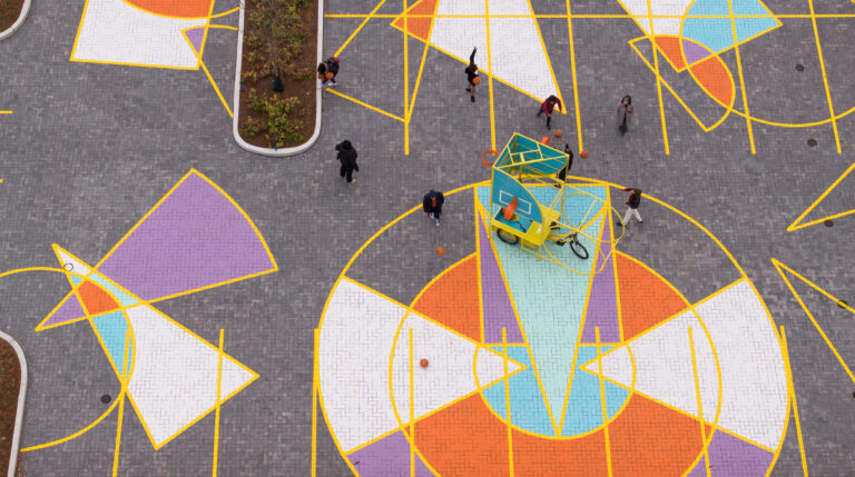 Seen from above, a white, purple, orange, and blue geometric mural turns a parking lot into a play space