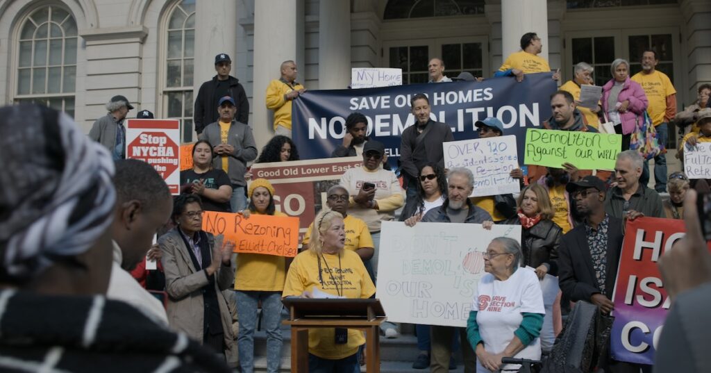 A woman in a yellow shirt leads a protest from a podium