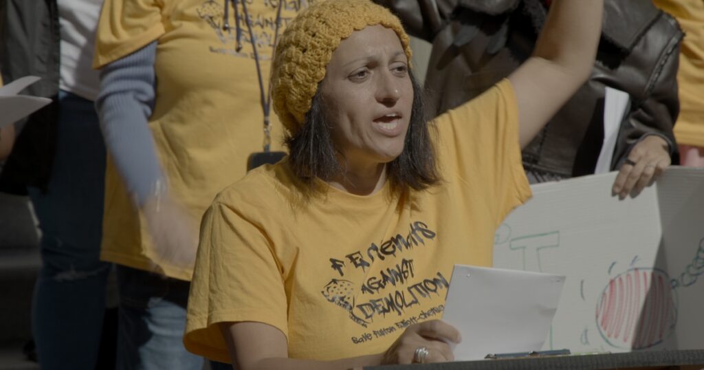 A woman in a yellow shirt that reads tenants against demolition