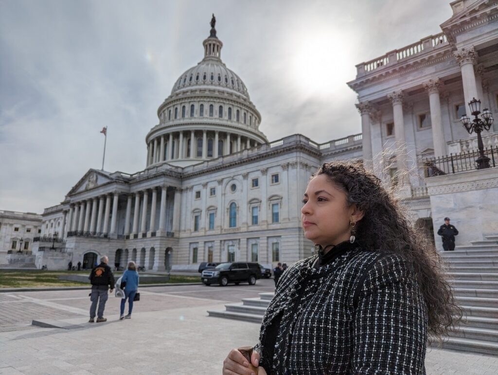 A woman stands to the right of the frame with the US Capitol building visible in the background