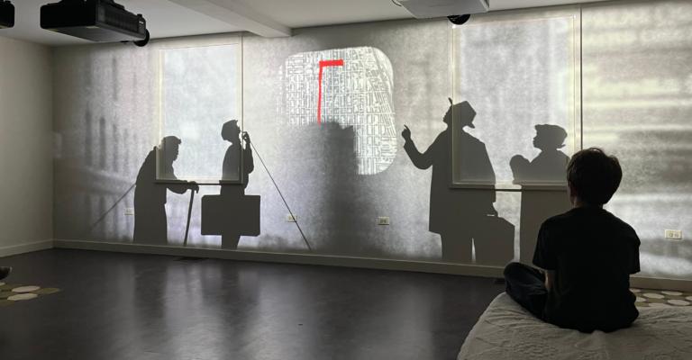 A map with a red line and silhouetted figures are projected on a wall