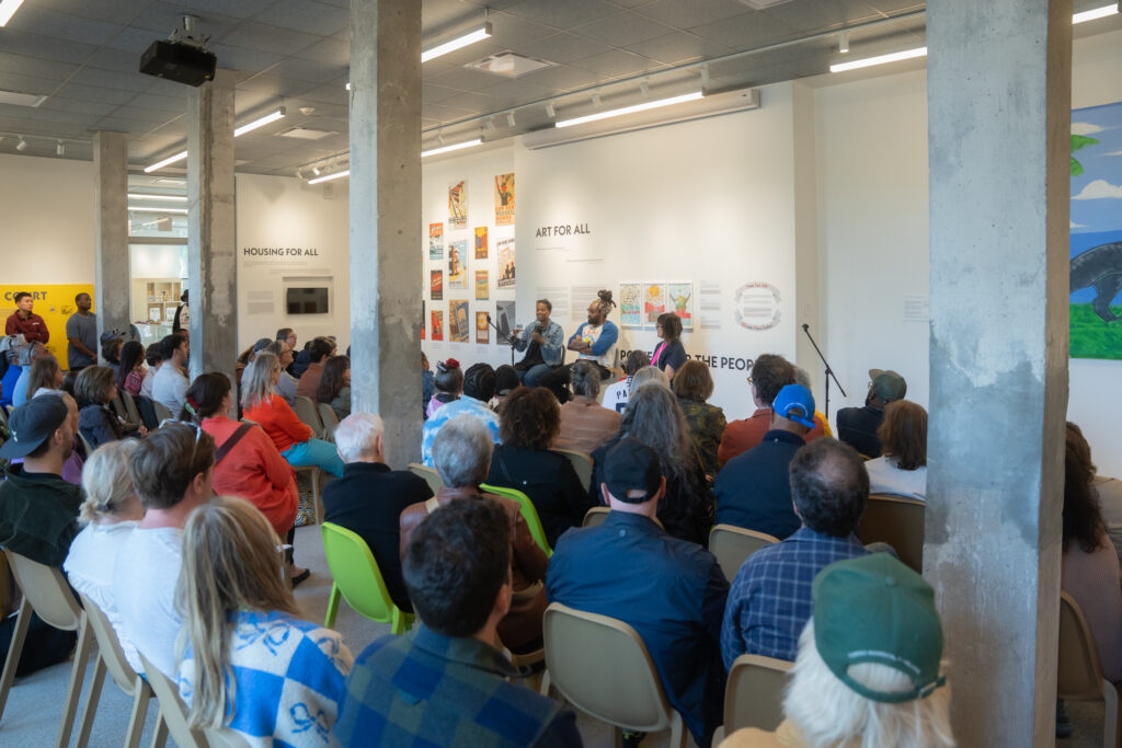 Panelists speaking to a seated audience in a gallery space