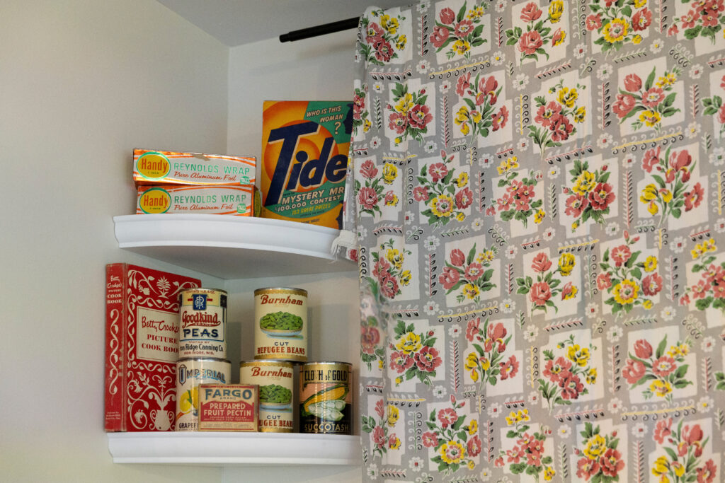 1969s kitchen vignette with canned goods and a cookbook and flower print curtain