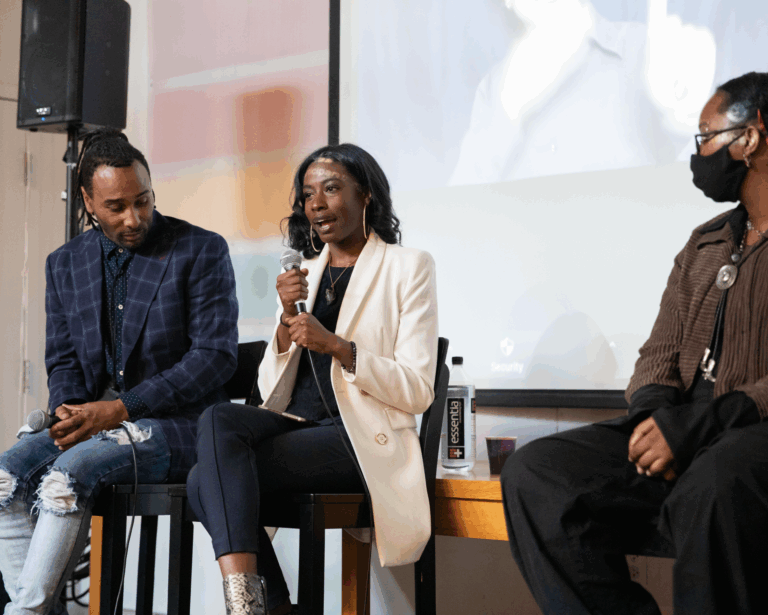 A person talks into a microphone while other panelists listen