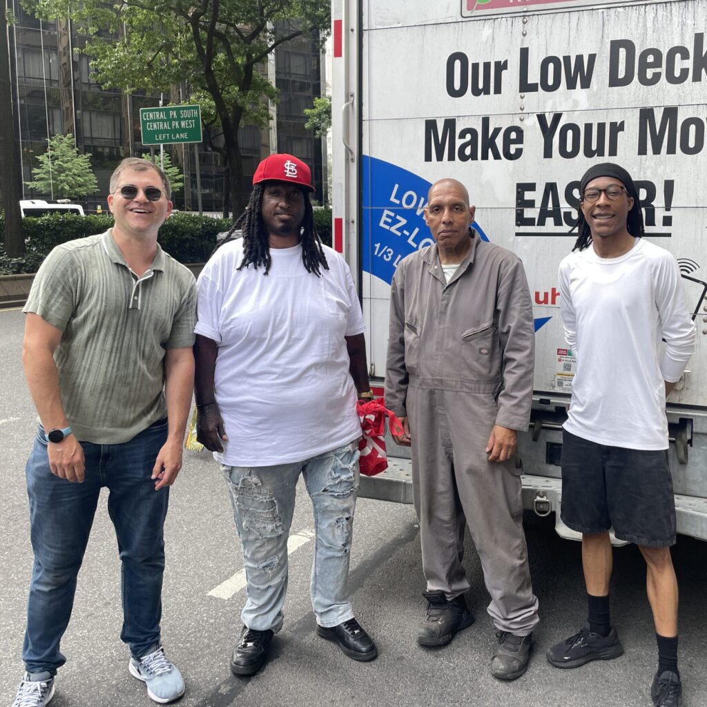 Four movers pose by the back of a truck