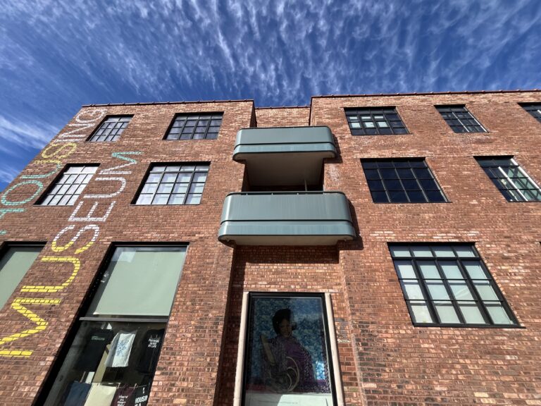 Looking upward at a three-story red brick building with turquoise balconies