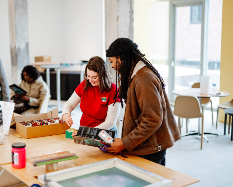 Two people pick up art supplies from a table