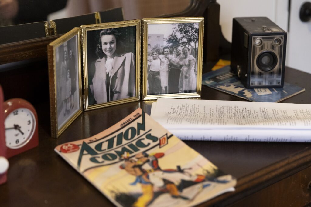 On top of a dresser, a collection of objects from the 1930s including a comic book, framed photos, and a vintage camera