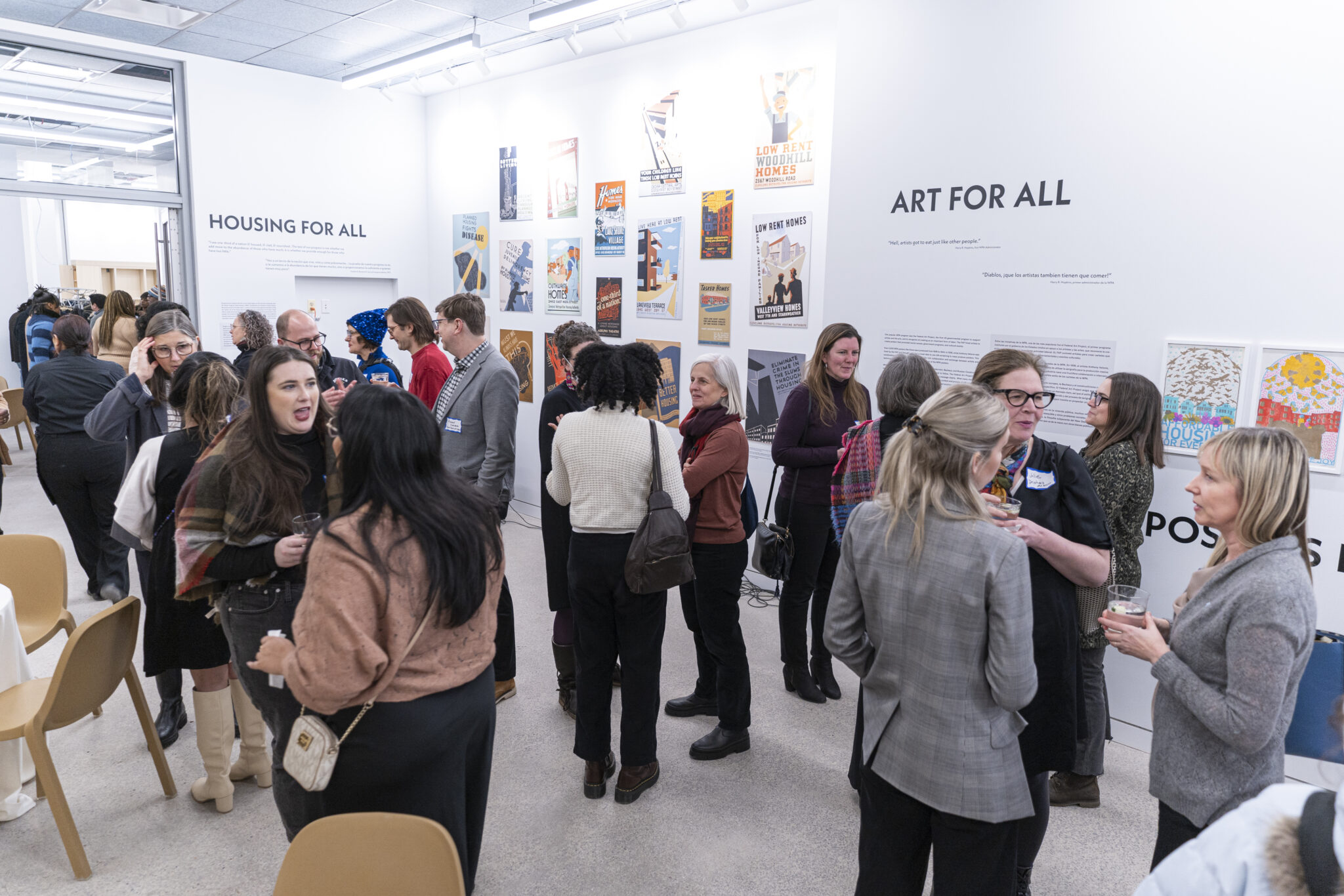 People socialize in an event space, with an exhibit visible on the walls