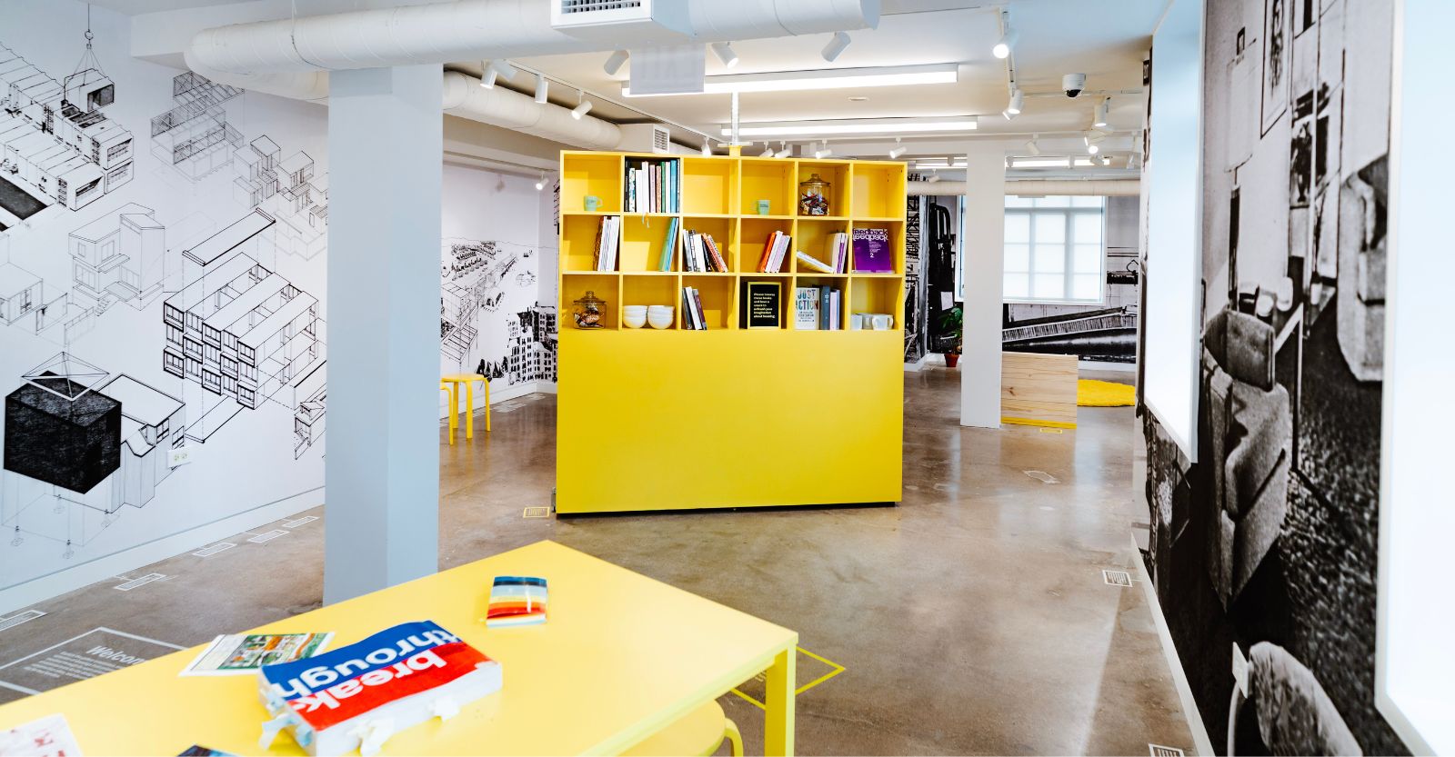 A yellow bookshelf in a gallery, with walls covered in historical photos and architectural drawings