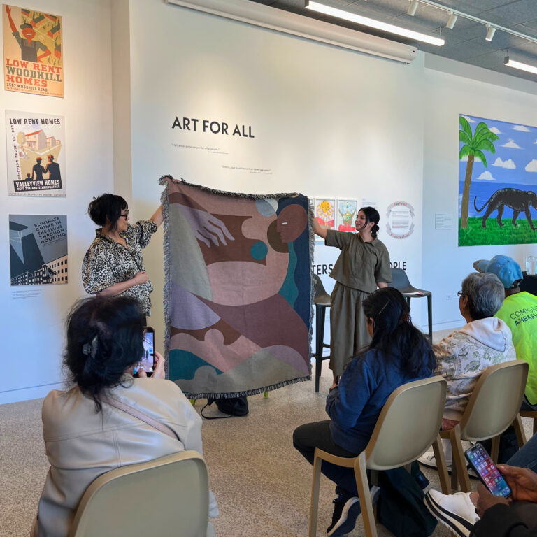 Two people hold up a modern tapestry in brown and greens