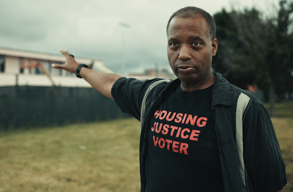 Film still of Don Washington in a shirt that reads Housing Justice Voter