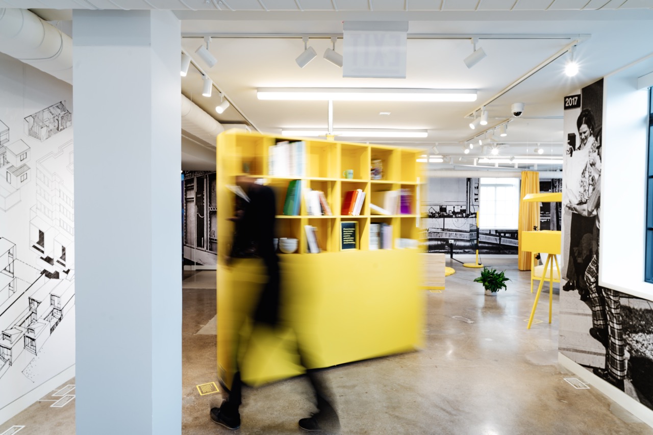 A person rotates a bright yellow shelf in a gallery