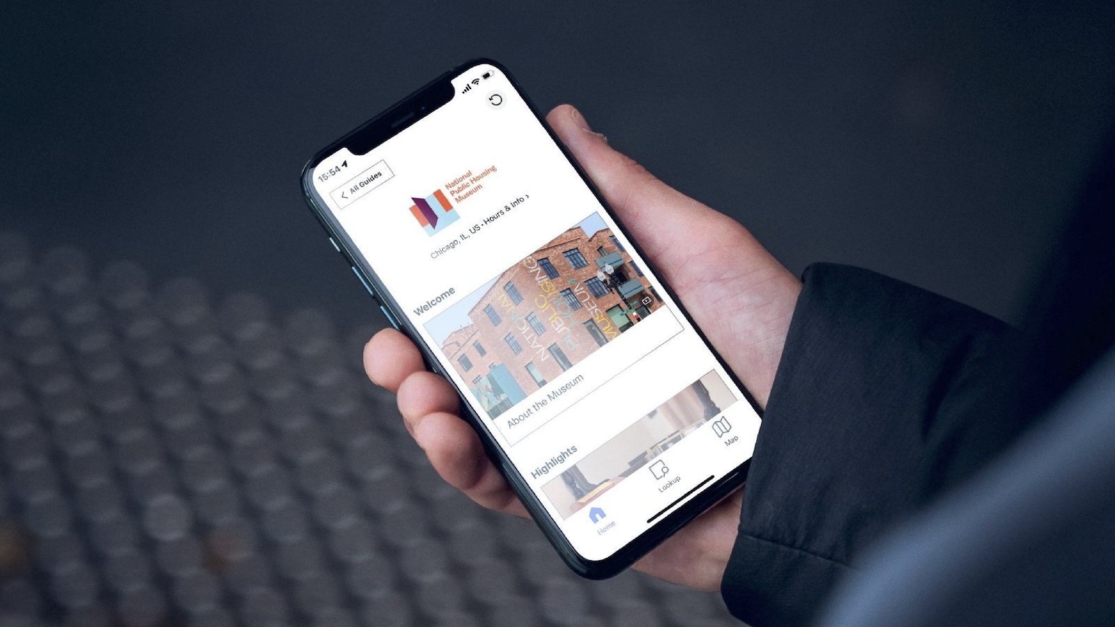 Over-the-shoulder view of someone holding a phone with the logo for the National Public Housing Museum visible on it