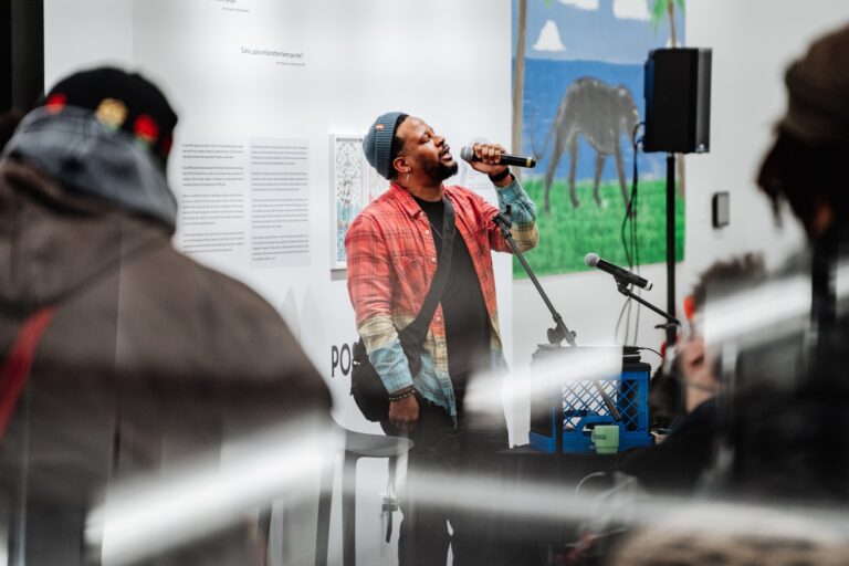 Open Mike Eagle at the microphone, with a painting of a panther in the background