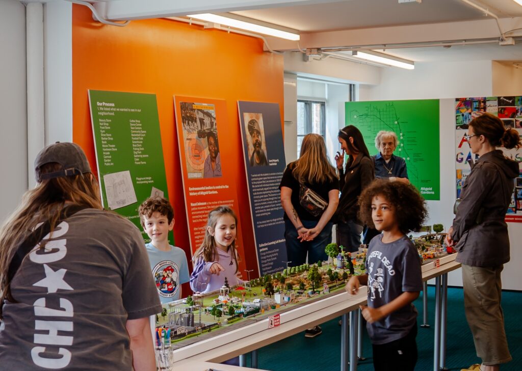 A group of kids gather around a long table with a diorama on top