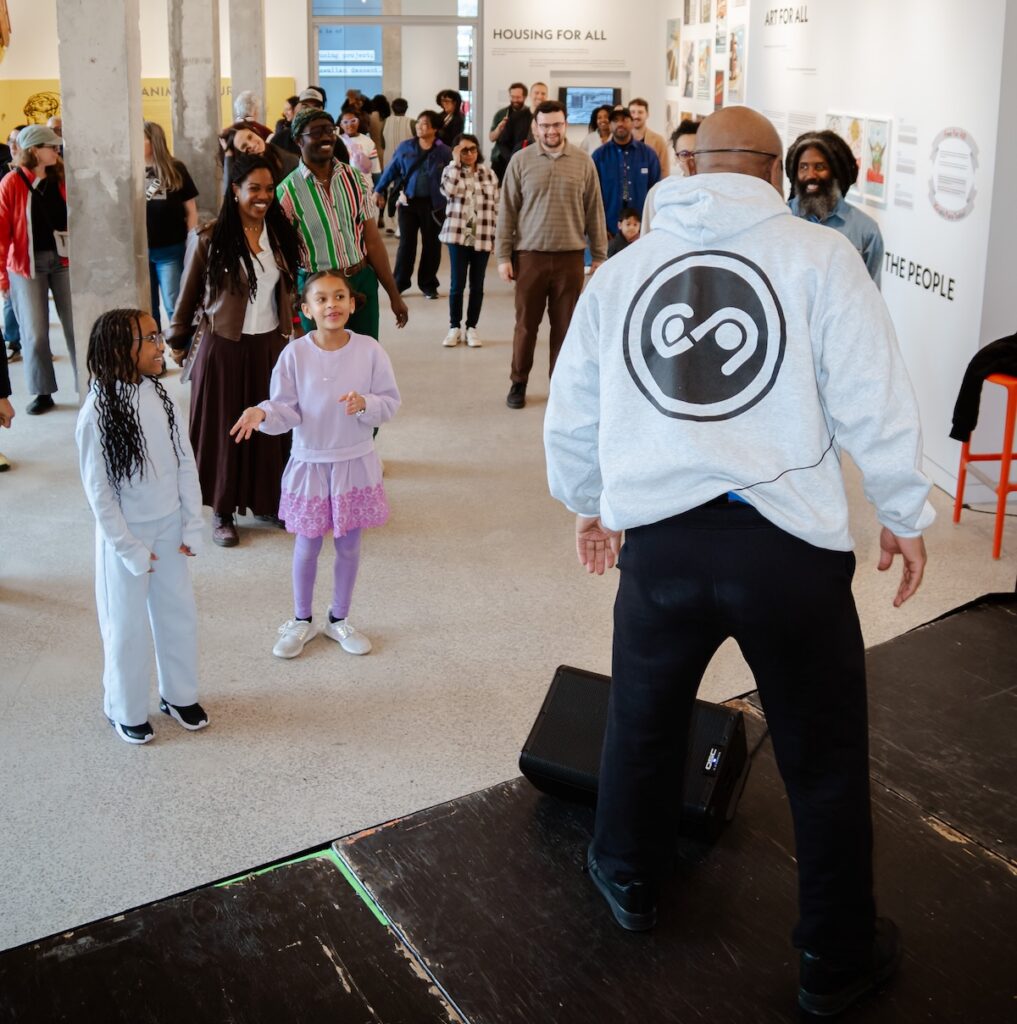 A dance instructor up on a stage in front of group of kids and parents