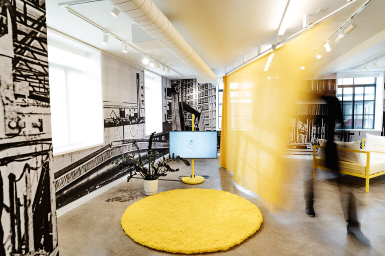 A person pulls a yellow curtain across a gallery space
