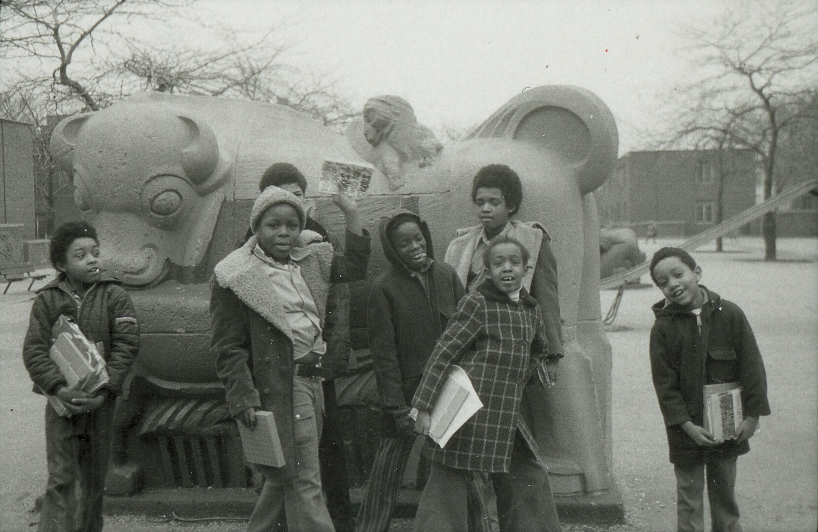 Vintage photo of seven kids posed with books and notebooks in front of an large animal sculpture