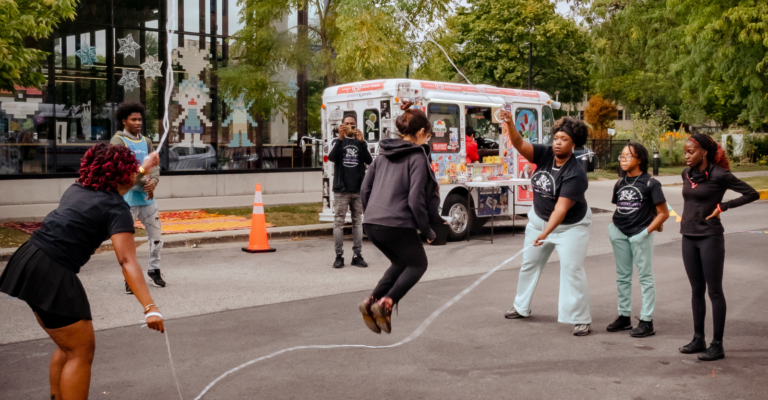 Playing double dutch jump rope on the street, with an ice cream truck in the background