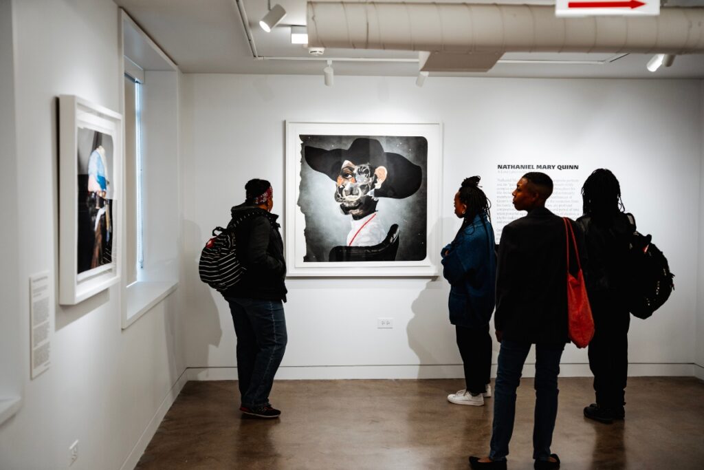 A group of people gather around a large portrait in a gallery