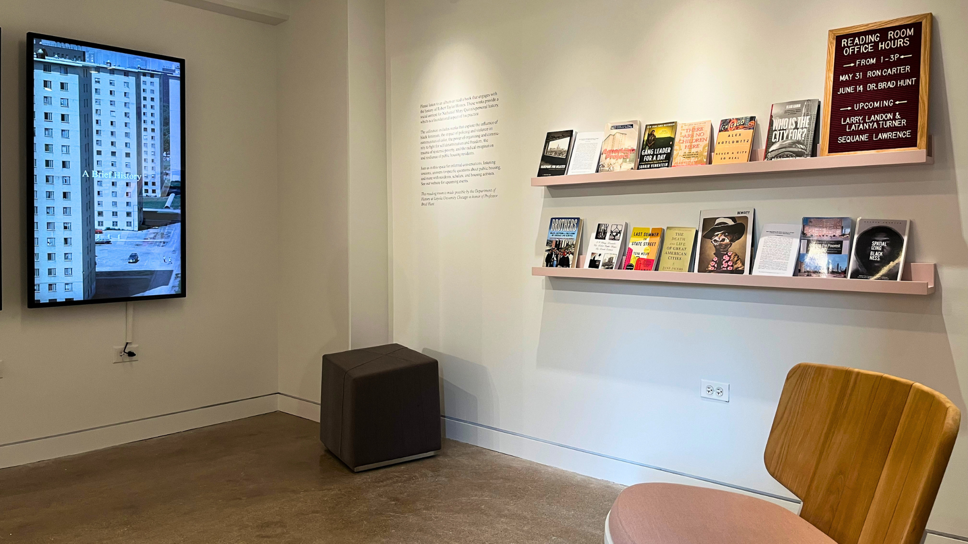 Installation view of resource room with books on a rail shelf, seating, and a digital screen