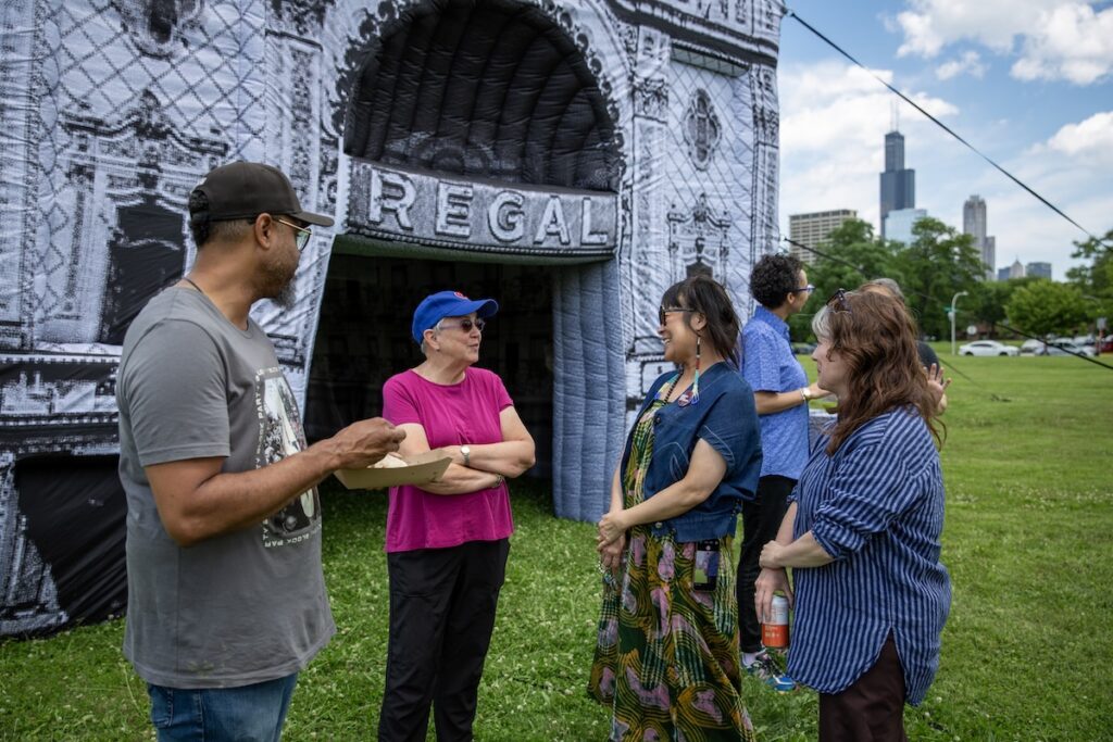 People eating and talking in front of an inflatable structure with the word Regal printed across an arched entranceway