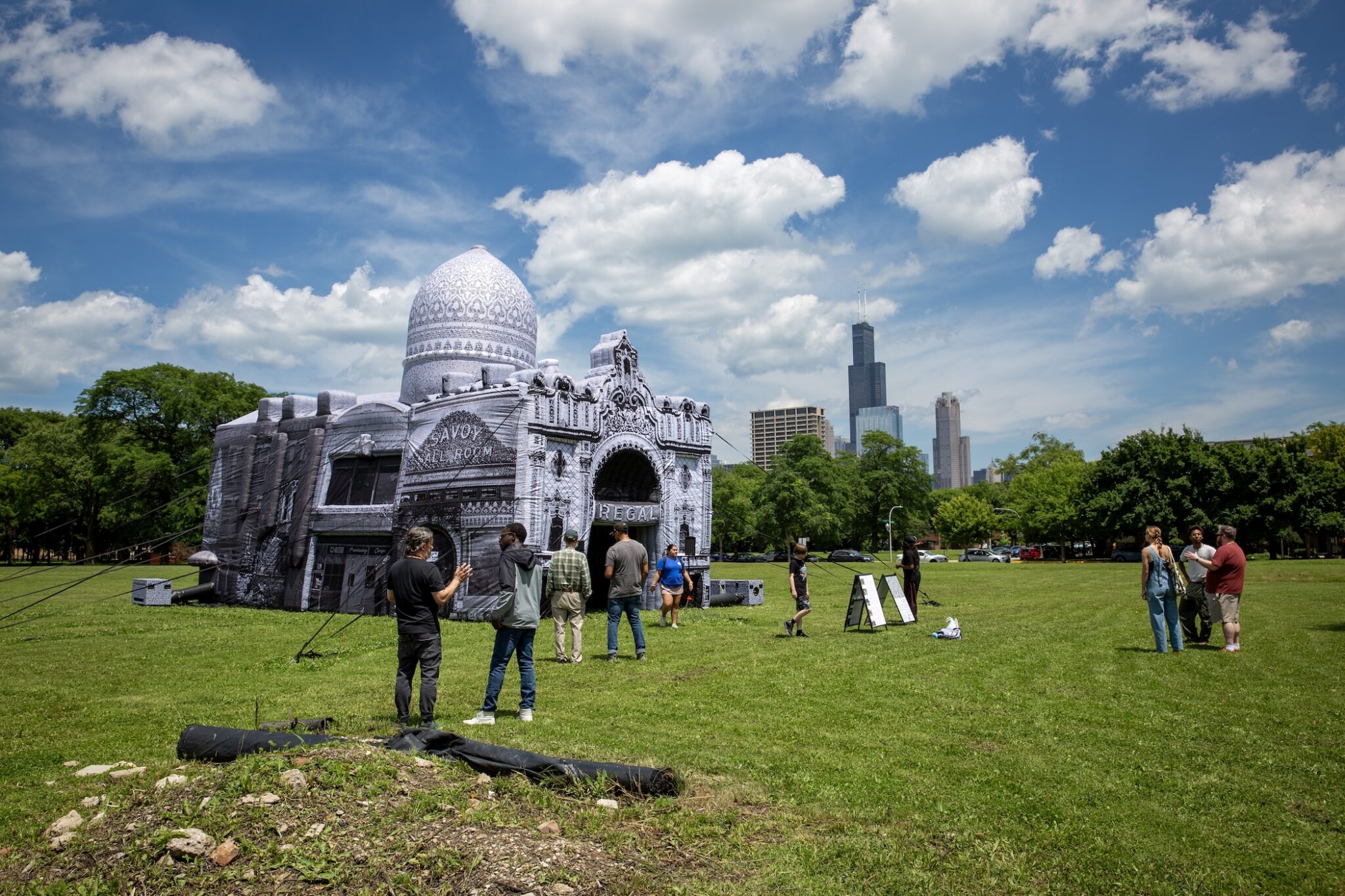 People gather in a field around a white inflatable building with the Chicago skyline in the distance