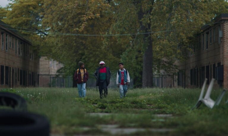 Still from the film We Grown Now, three kids walking through the grounds of a housing complex