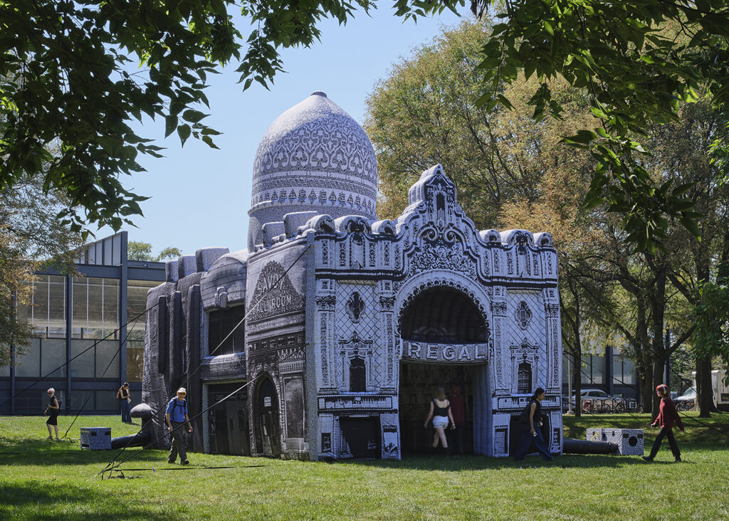 People walk around an inflatable architectural structure on a campus lawn