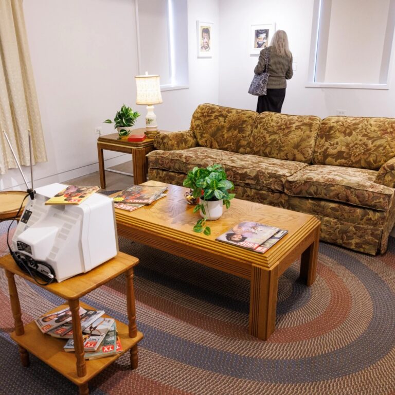 A vintage living room vignette in an art gallery, with a person looking at paintings in the background