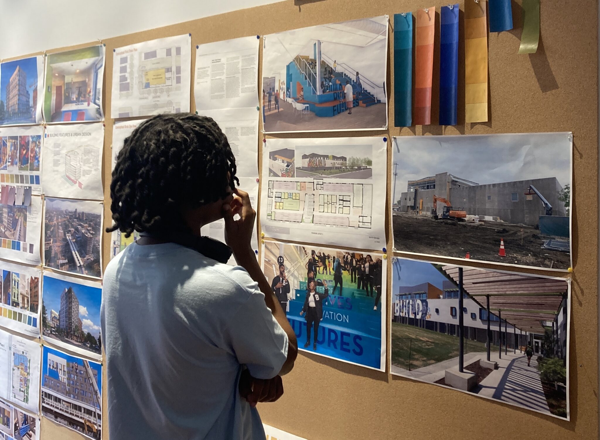From behind, a person looking at a cork board with pinned up architectural plans and renderings