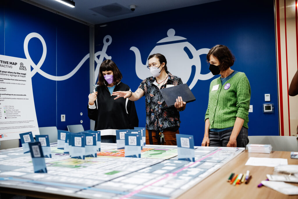 Three people stand and look at the map, with the middle person gesturing to it.