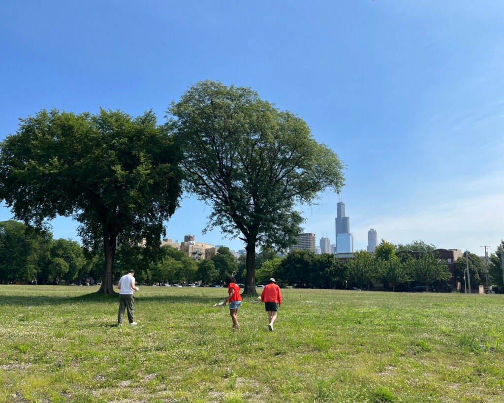 Three people walking through an open field with the Chicago skyline in the background